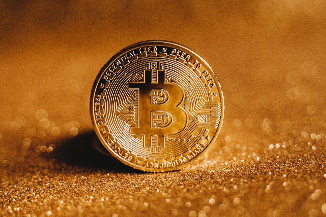 A detailed close-up of a shiny gold Bitcoin coin resting on a glittery surface.